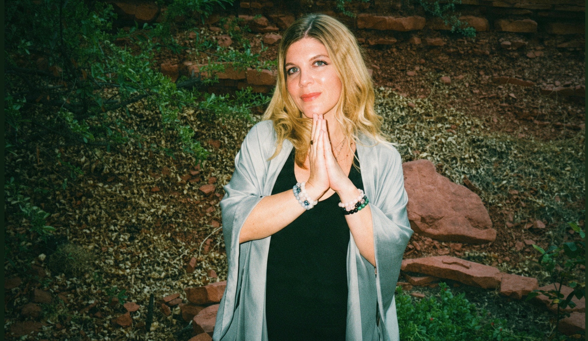 Lisa Gray with her hands at her heart, surrounded by greenery and red rocks